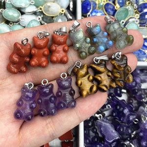 May include: A collection of gemstone gummy bear charms in various colors, including amethyst, tiger's eye, red jasper, and labradorite. The charms are strung on silver chains and are perfect for jewelry making.