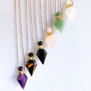 May include: Seven gold chain necklaces with crystal gemstone pendants. Each pendant is a clear glass bottle with a gold stopper and a crystal gemstone cap. The gemstones are amethyst, tiger's eye, black onyx, rose quartz, green aventurine, and clear quartz.