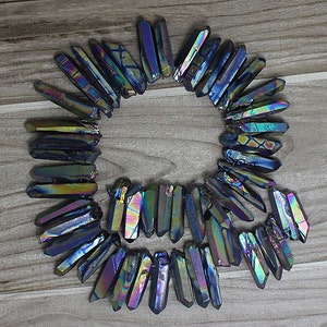 Könnte beinhalten: Eine Sammlung von regenbogenfarbenen schwarzen Kristallspitzen, auch bekannt als Titan-Aura-Quarz, die in einem Kreis auf einer Holzoberfläche angeordnet sind. Die Kristalle haben einen Regenbogen-Schimmer und sind etwa 2,5 bis 5 cm lang.