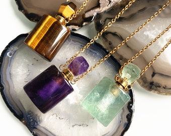 Puede incluir: Tres collares de cadena dorada con colgantes de botella de cristal. Las botellas están hechas de ojo de tigre, amatista y fluorita verde.