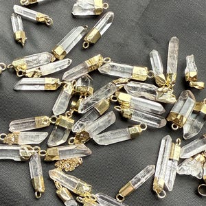 May include: A collection of clear quartz crystal points with gold-toned metal caps. The points are various sizes and shapes, and some have a chain attached.