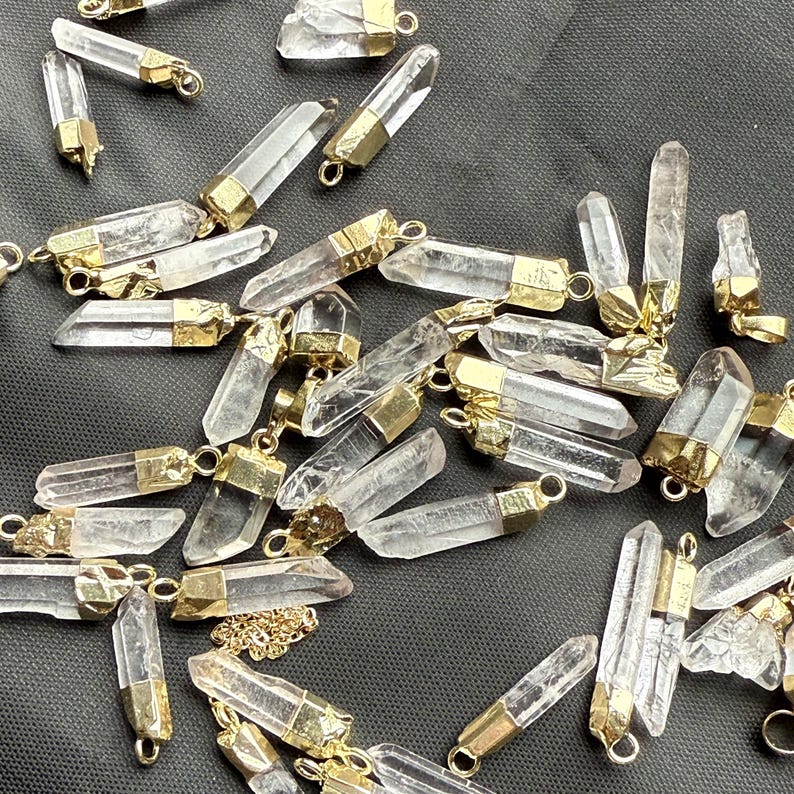 May include: A collection of clear quartz crystal points with gold-toned metal caps. The points are various sizes and shapes, and some have a chain attached.