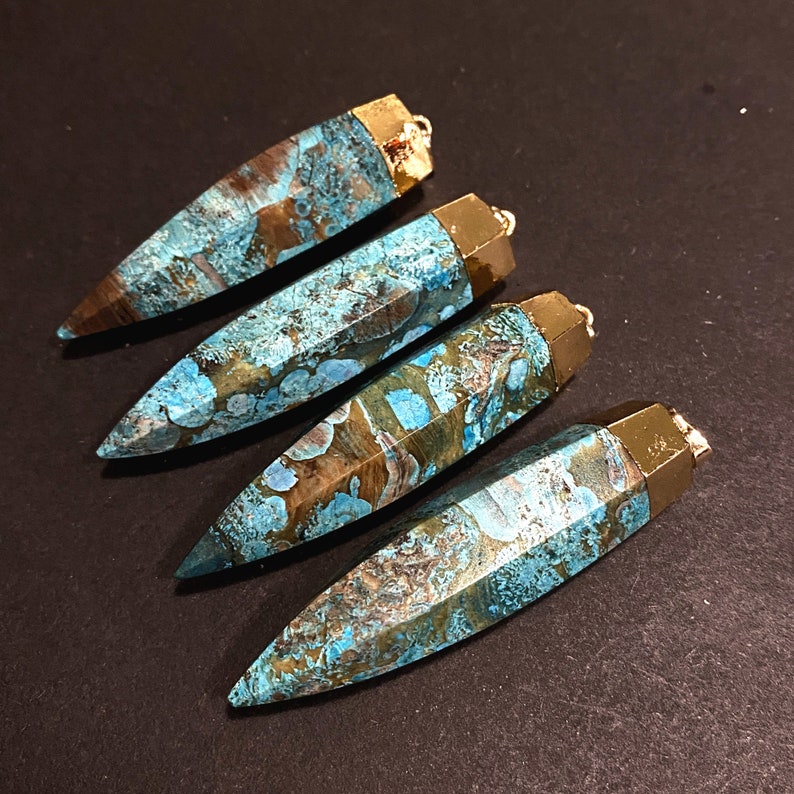 May include: Four turquoise and brown agate gemstone pendants with gold-toned metal caps and loops. The pendants are shaped like long, pointed teardrops.