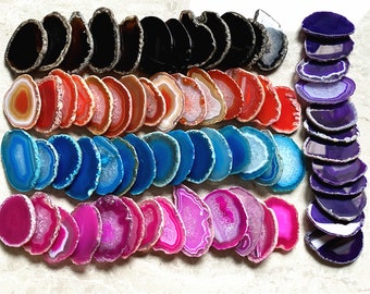Op de afbeelding: Assortiment van agaatplakken in verschillende kleuren, waaronder paars, blauw, roze, rood en zwart. De plakken zijn in rijen gerangschikt, met de paarse plakken aan de rechterkant van de afbeelding.