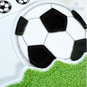 May include: A white soccer ball with black stitching is on a green grass-like surface. The ball is partially visible, with the top half of the ball showing.