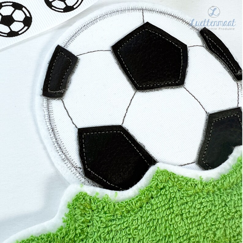 May include: A white soccer ball with black stitching is on a green grass-like surface. The ball is partially visible, with the top half of the ball showing.