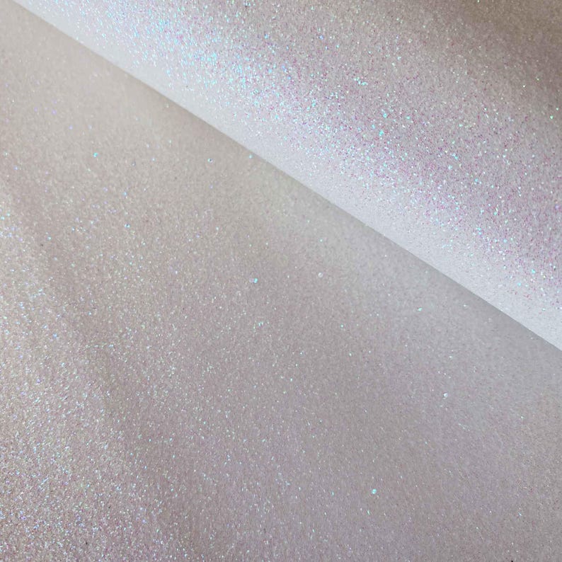 May include: White iridescent glitter fabric with a subtle shimmer. The fabric is folded in half, showing the texture of the glitter.