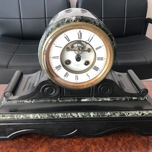May include: A black and green marble mantel clock with a white face and gold hands. The clock has a Roman numeral dial and a decorative base.