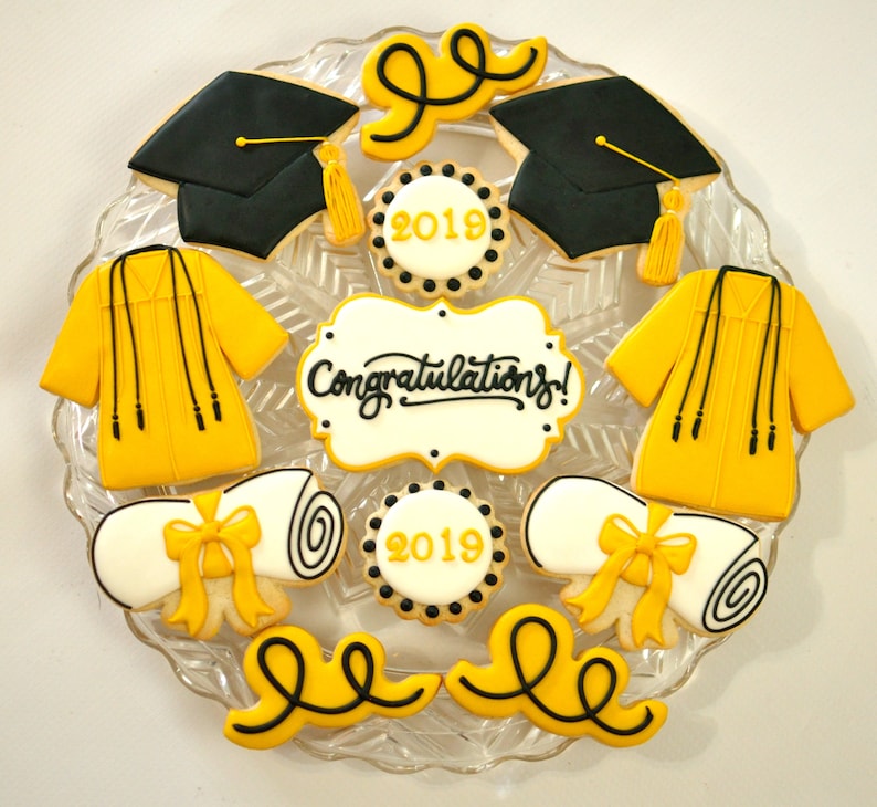 May include: A set of nine graduation-themed sugar cookies decorated with yellow and black icing. The cookies feature a graduation cap, a diploma, a gown, and the text "Congratulations!" and "2019".