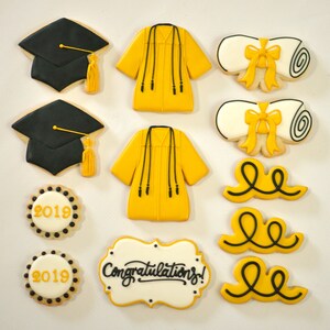 May include: A set of graduation-themed sugar cookies. The cookies are decorated with yellow and black frosting. The set includes two graduation caps, two graduation gowns, two diplomas, three curly ribbons, and two round cookies with the years 2018 and 2019. One cookie has the text "Congratulations!" in black frosting.