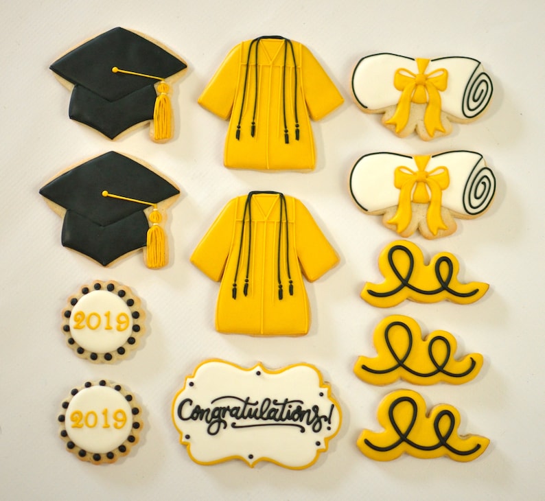 May include: A set of graduation-themed sugar cookies. The cookies are decorated with yellow and black frosting. The set includes two graduation caps, two graduation gowns, two diplomas, three curly ribbons, and two round cookies with the years 2018 and 2019. One cookie has the text "Congratulations!" in black frosting.