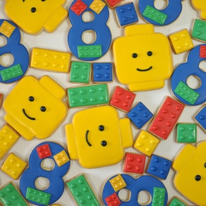 May include: Assortment of colorful, decorated sugar cookies shaped like Lego bricks and numbers. The cookies feature various designs, including smiley faces, numbers, and Lego brick patterns.