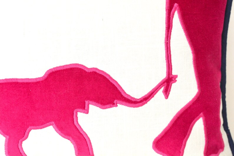 Op de afbeelding: Een wit kussen met een roze geborduurd ontwerp van twee olifanten. De grotere olifant staat en de kleinere olifant loopt naar de grotere olifant.