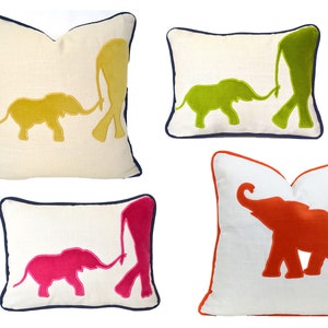 Op de afbeelding: Vier decoratieve kussens met geborduurde olifantensilhouetten. De kussens zijn wit met een marineblauwe rand. De olifanten zijn in verschillende kleuren: geel, groen, roze en oranje.
