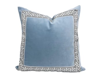 May include: A blue velvet throw pillow with a white and gray Greek key border.