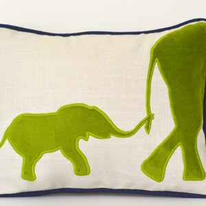 Op de afbeelding: Een wit kussen met een donkerblauwe rand heeft een appliqu&eacute;-ontwerp met twee groene olifanten. De grotere olifant loopt en de kleinere olifant volgt hem, verbonden door hun slurf.