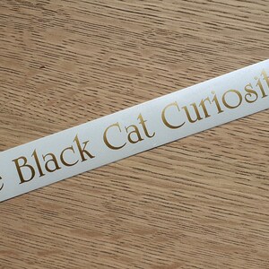 May include: White sticker with gold lettering that reads "Ye Olde Black Cat Curiosity Shop".