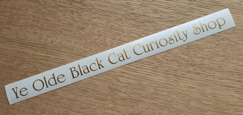 May include: White sticker with gold lettering that reads "Ye Olde Black Cat Curiosity Shop".