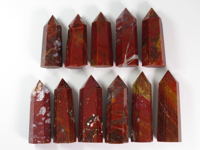 May include: A collection of 15 red, brown, and white jasper crystal points. The points are arranged in two rows, with the points in the top row slightly offset from the points in the bottom row.