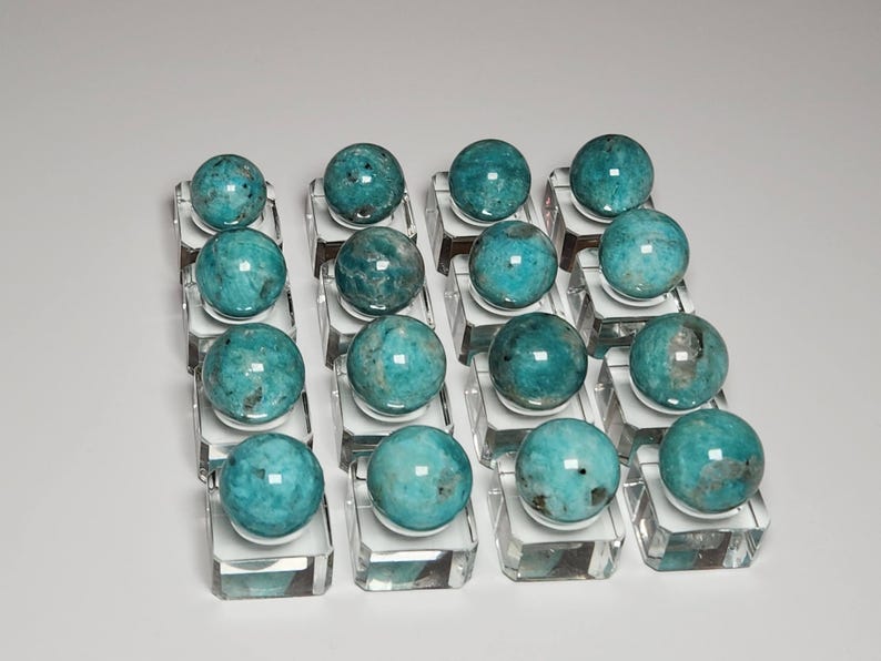 May include: A collection of 18 teal blue and green amazonite spheres displayed on clear glass bases.