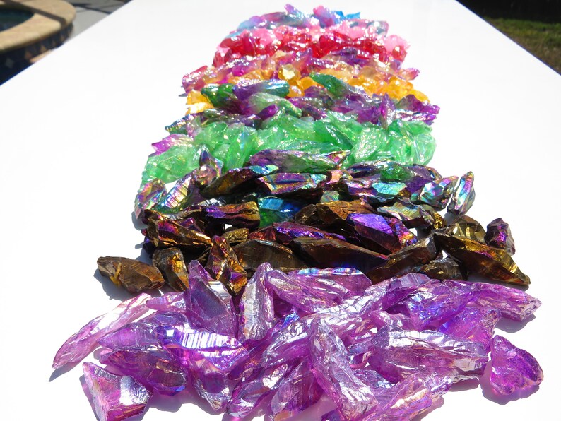 May include: A rainbow assortment of iridescent crystal points. The crystals are arranged in a rainbow order, from red to purple. The crystals are all different sizes and shapes.