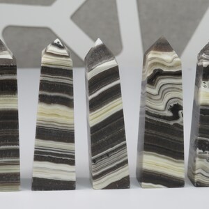 May include: Five black and white striped obelisk shaped crystal points. The points are polished and have a smooth, glossy finish.