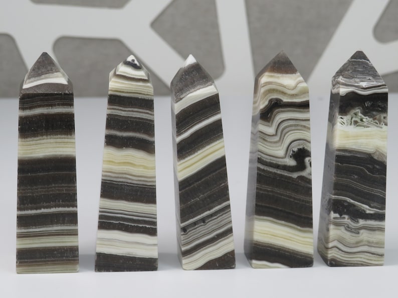 May include: Five black and white striped obelisk shaped crystal points. The points are polished and have a smooth, glossy finish.