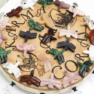 May include: A wooden round tray with the words "Karma and Co" engraved on it. The tray is decorated with 20 small dragonfly carvings made of various types of stones, including pink, green, white, black, and red.