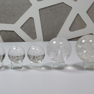 May include: Five clear quartz crystal spheres of varying sizes, displayed on small square bases. The spheres are smooth and translucent, with a slight sparkle.