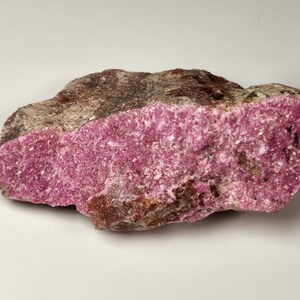 May include: A rough, pink and brown rock with a crystalline texture. The rock has a pink, sparkly surface and a brown, rough underside.