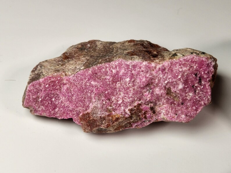 May include: A rough, pink and brown rock with a crystalline texture. The rock has a pink, sparkly surface and a brown, rough underside.