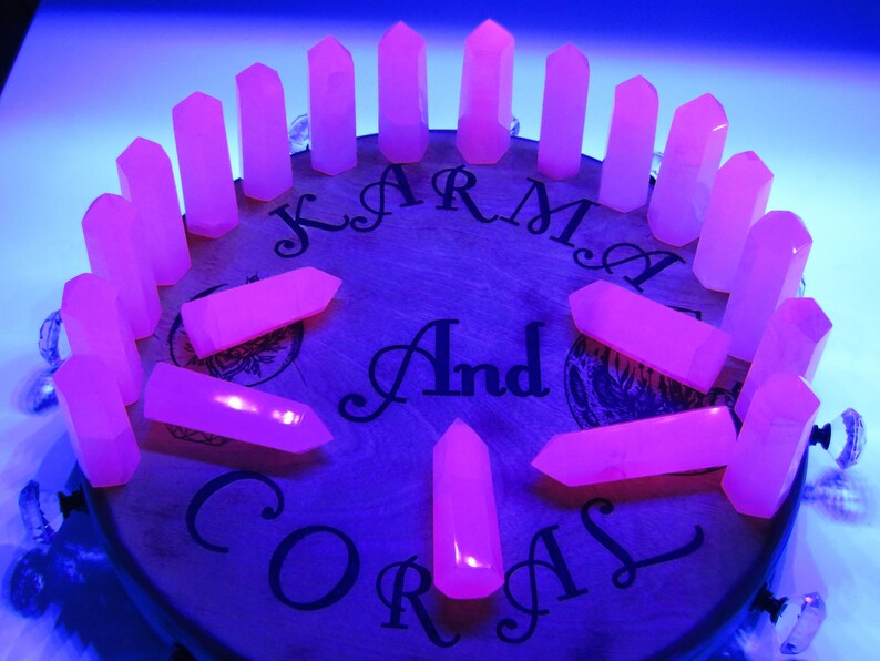 May include: A collection of 18 pink crystal points arranged in a circle on a wooden surface. The surface has the words "Karma And Coral" printed on it.
