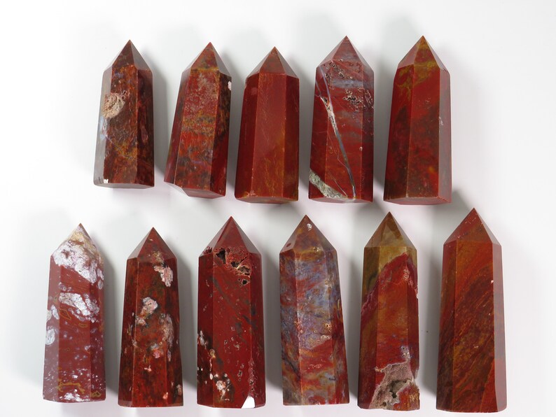 May include: Twelve red jasper crystal points with varying shades of red, brown, and white. The points are all approximately the same size and shape.