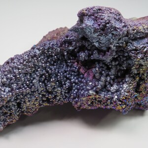 May include: A large, iridescent purple and silver goethite specimen with a rough, bubbly texture. The mineral has a metallic sheen and displays a variety of colors, including purple, blue, and green.
