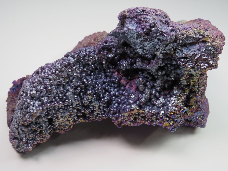 May include: A large, iridescent purple and silver goethite specimen with a rough, bubbly texture. The mineral has a metallic sheen and displays a variety of colors, including purple, blue, and green.