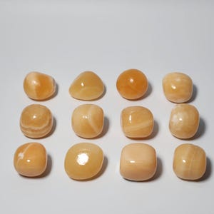 May include: A collection of 12 smooth, polished orange calcite tumbled stones. The stones are various shapes and sizes, with some having a more rounded shape and others being more square.