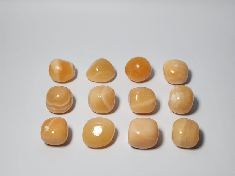 May include: A collection of 12 smooth, polished orange calcite tumbled stones. The stones are various shapes and sizes, with some having a more rounded shape and others being more square.