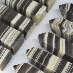 May include: A collection of black and white striped polished stone points. The points are all different sizes and shapes, but they all have a similar pattern of black and white stripes.