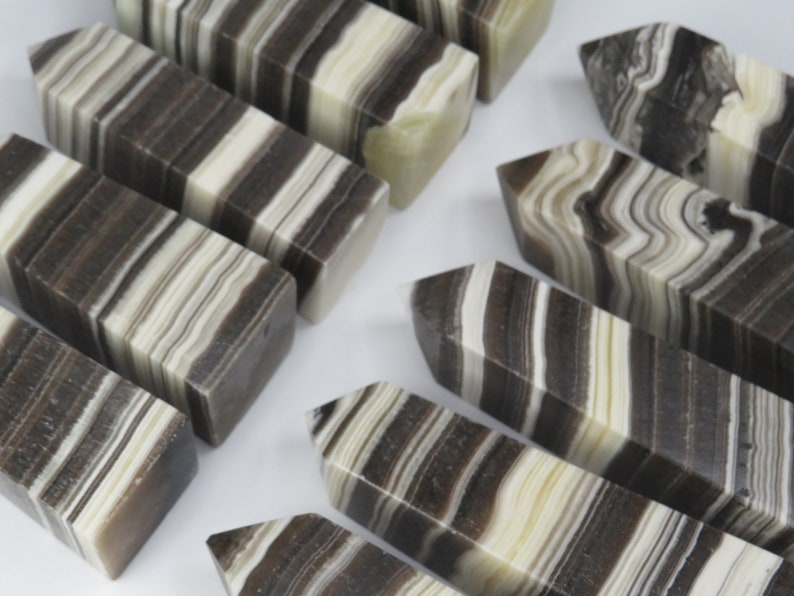 May include: A collection of black and white striped polished stone points. The points are all different sizes and shapes, but they all have a similar pattern of black and white stripes.
