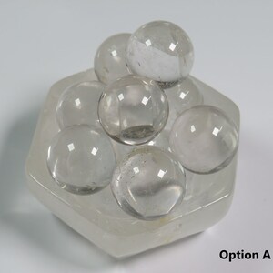 May include: A clear quartz crystal cluster with eight smooth, round spheres arranged in a hexagonal base. The crystal cluster is made of clear quartz and has a natural, polished finish.
