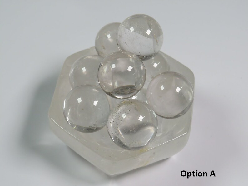 May include: A clear quartz crystal cluster with eight smooth, round spheres arranged in a hexagonal base. The crystal cluster is made of clear quartz and has a natural, polished finish.