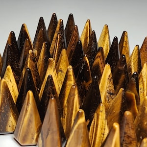 Può includere: Un gruppo di punte di cristallo di occhio di tigre di colore marrone dorato e nero disposte in una formazione appuntita. Le punte sono tutte più o meno della stessa dimensione e forma, e sono disposte in modo da creare una sensazione di movimento ed energia.