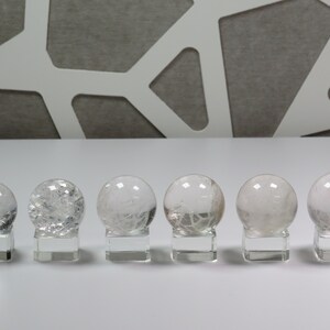 May include: Six clear quartz crystal spheres on individual stands. The spheres are all different sizes and have a cloudy, translucent appearance.