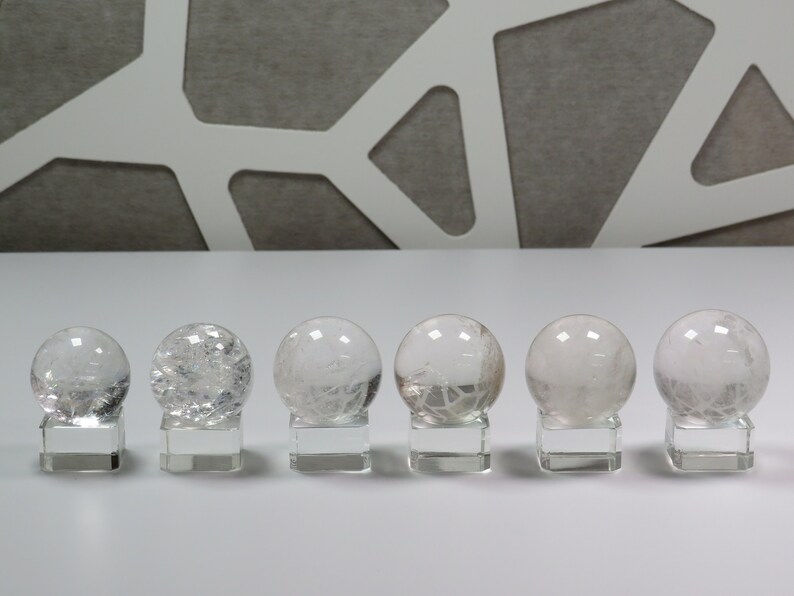 May include: Six clear quartz crystal spheres on individual stands. The spheres are all different sizes and have a cloudy, translucent appearance.