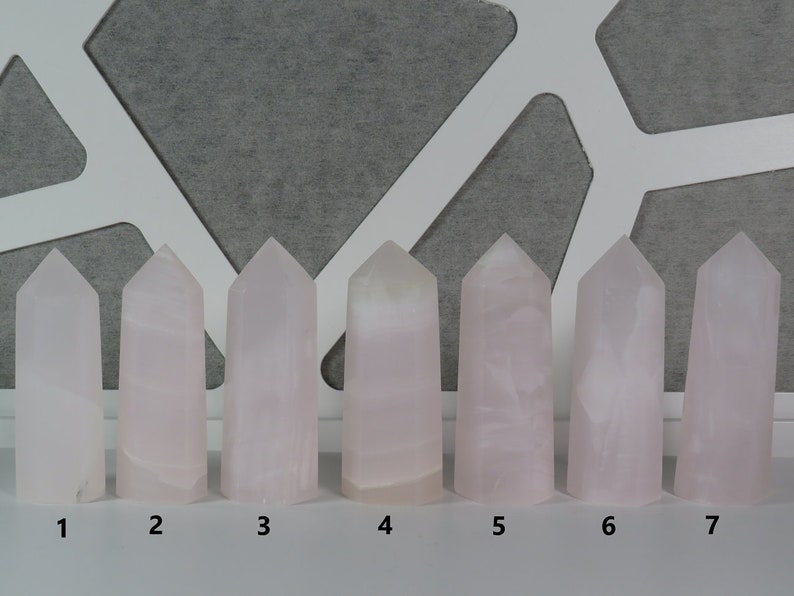 May include: Seven pink crystal points, numbered 1 through 7, arranged in a row on a white surface. The crystals are all roughly the same size and shape, with a pointed top and a flat base.