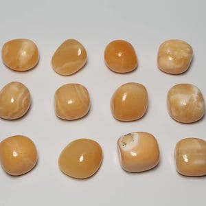 May include: Twelve tumbled orange calcite stones with white veining. The stones are smooth and polished.