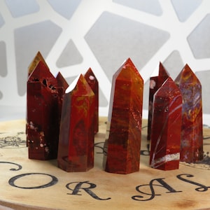 May include: A group of ten red and orange agate crystal points arranged on a wooden base with the word "CORAL" printed on it.