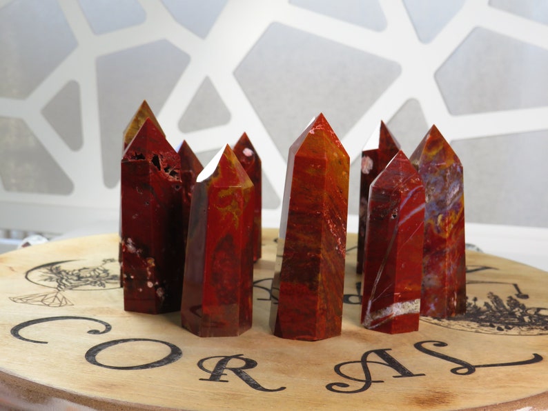 May include: A group of ten red and orange agate crystal points arranged on a wooden base with the word "CORAL" printed on it.