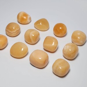 May include: A collection of twelve tumbled carnelian stones. The stones are a light orange color with some white streaks. They are smooth and polished.