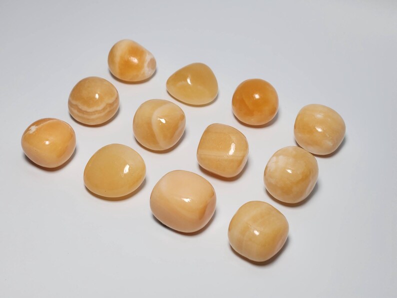 May include: A collection of twelve tumbled carnelian stones. The stones are a light orange color with some white streaks. They are smooth and polished.